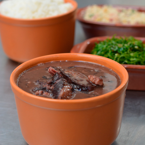 Feijoada servida em panelas de barro com arroz, farofa e couve